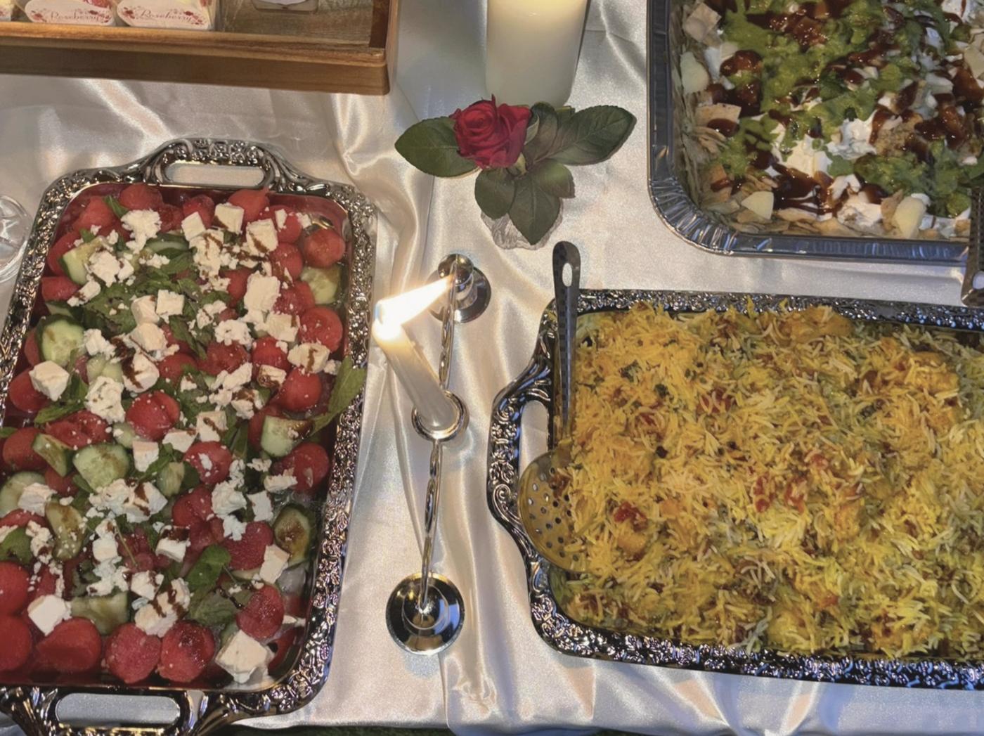 Silver trays of watermelon salad and golden rice with a rose and candle